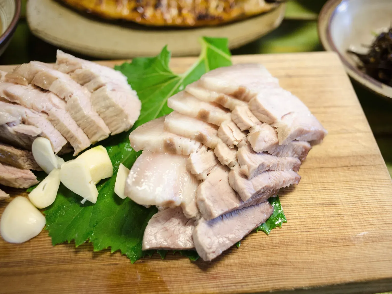 Sliced boiled pork belly on a wooden board with perilla leaves and garlic
