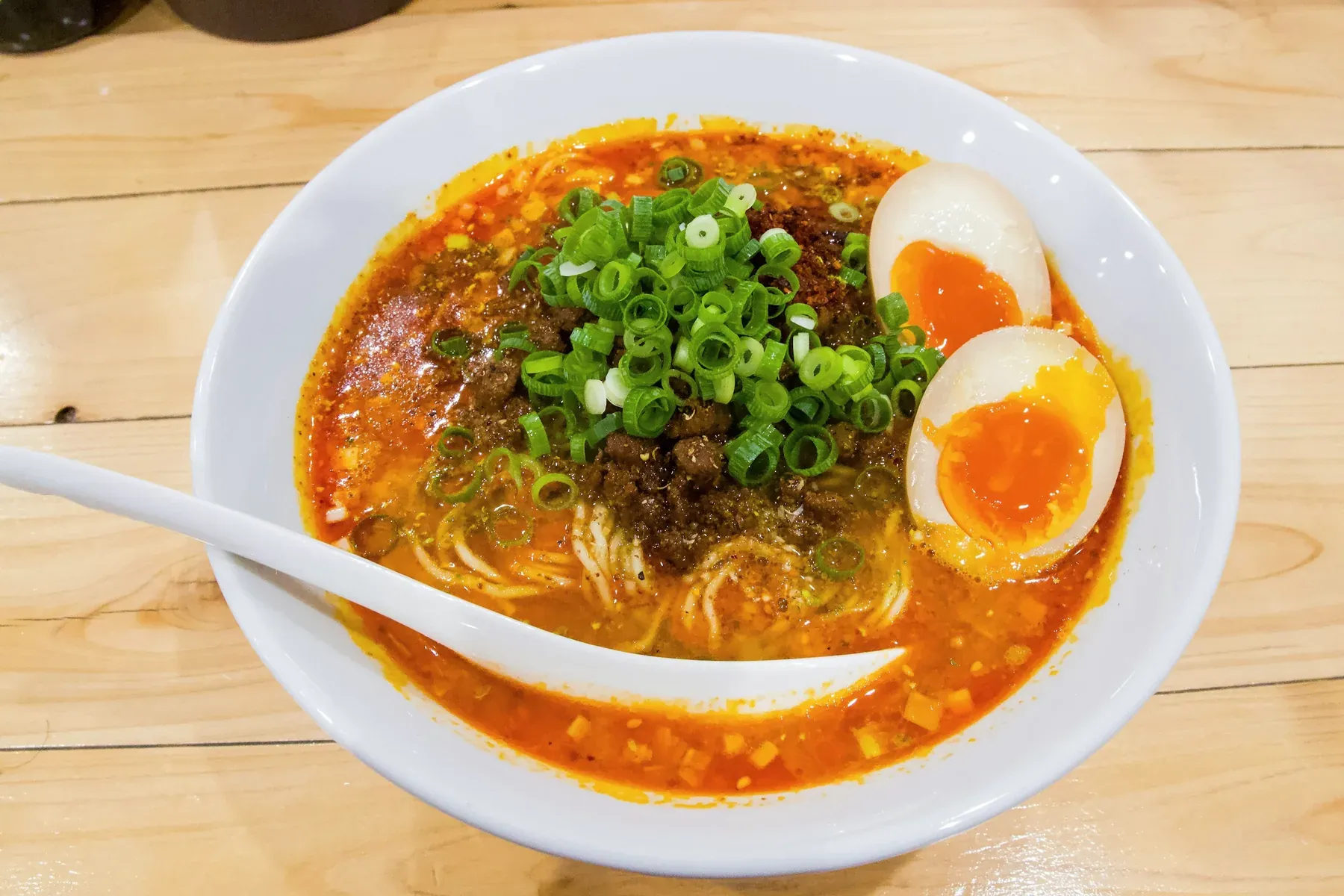 Red sesame tantan ramen in a white bowl with minced pork, a heap of scallions and two halved soft eggs