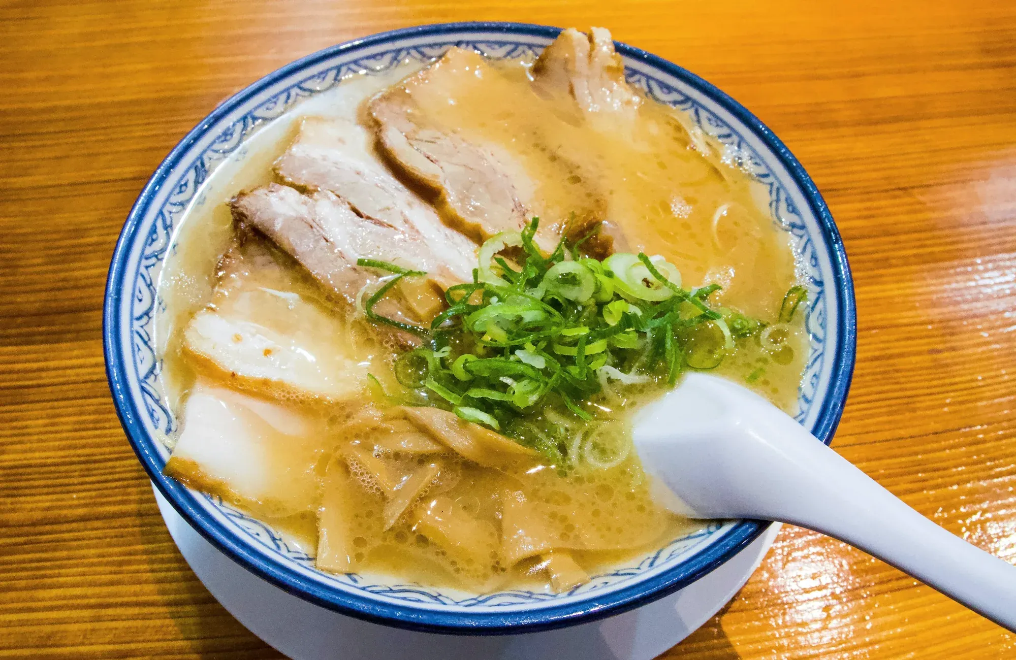 Creamy tonkotsu ramen in a blue-patterned bowl, heaped with chashu slices, bamboo shoots and scallions