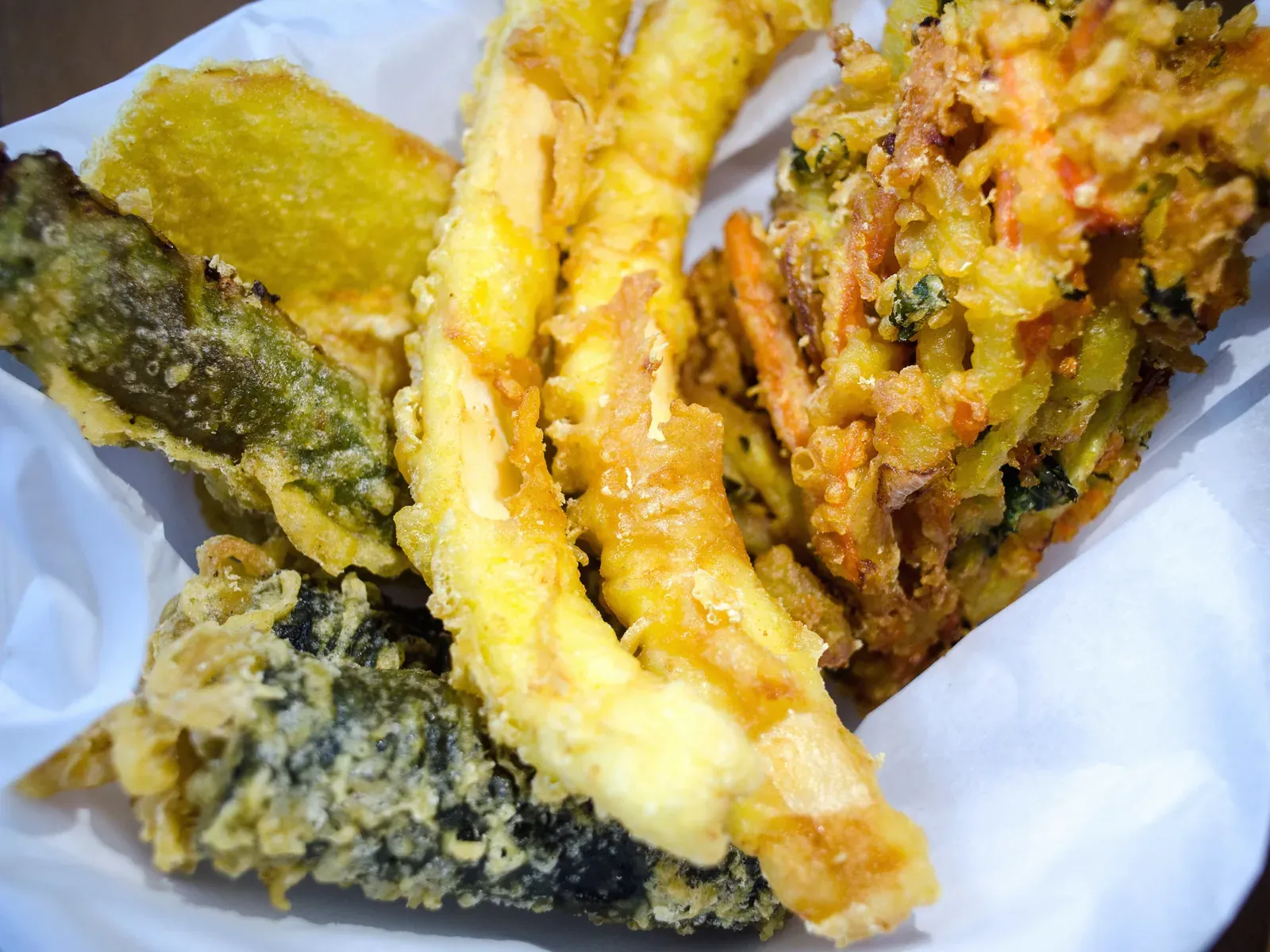 A paper-lined basket of fried seaweed rolls, squid, sweet potato and green chili