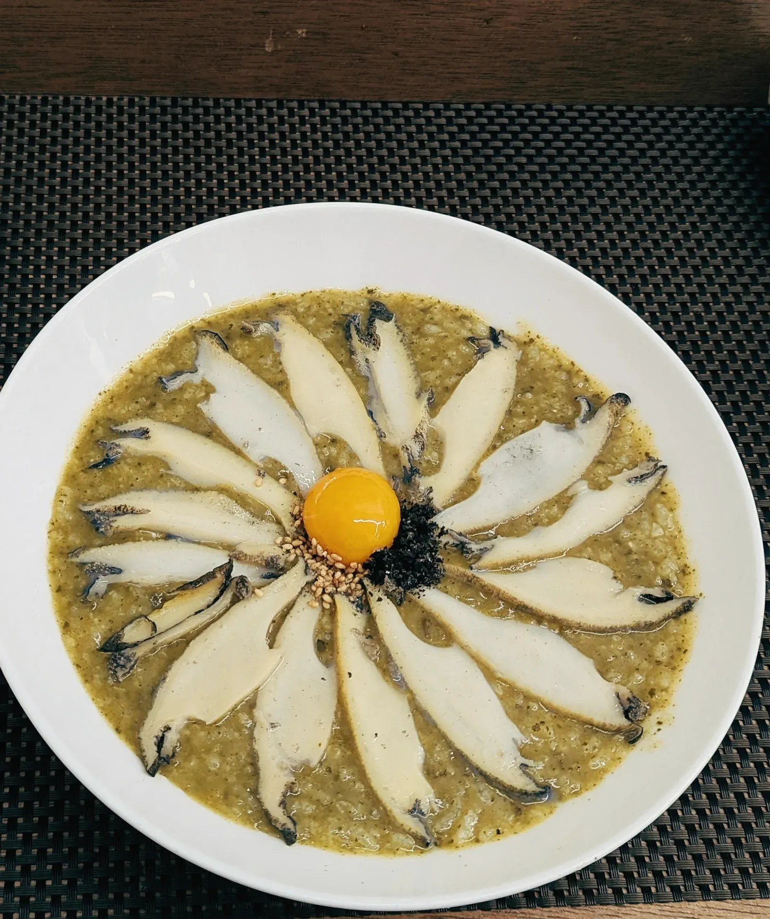 Green abalone porridge with fanned slices of abalone around an egg yolk, in a wide white bowl