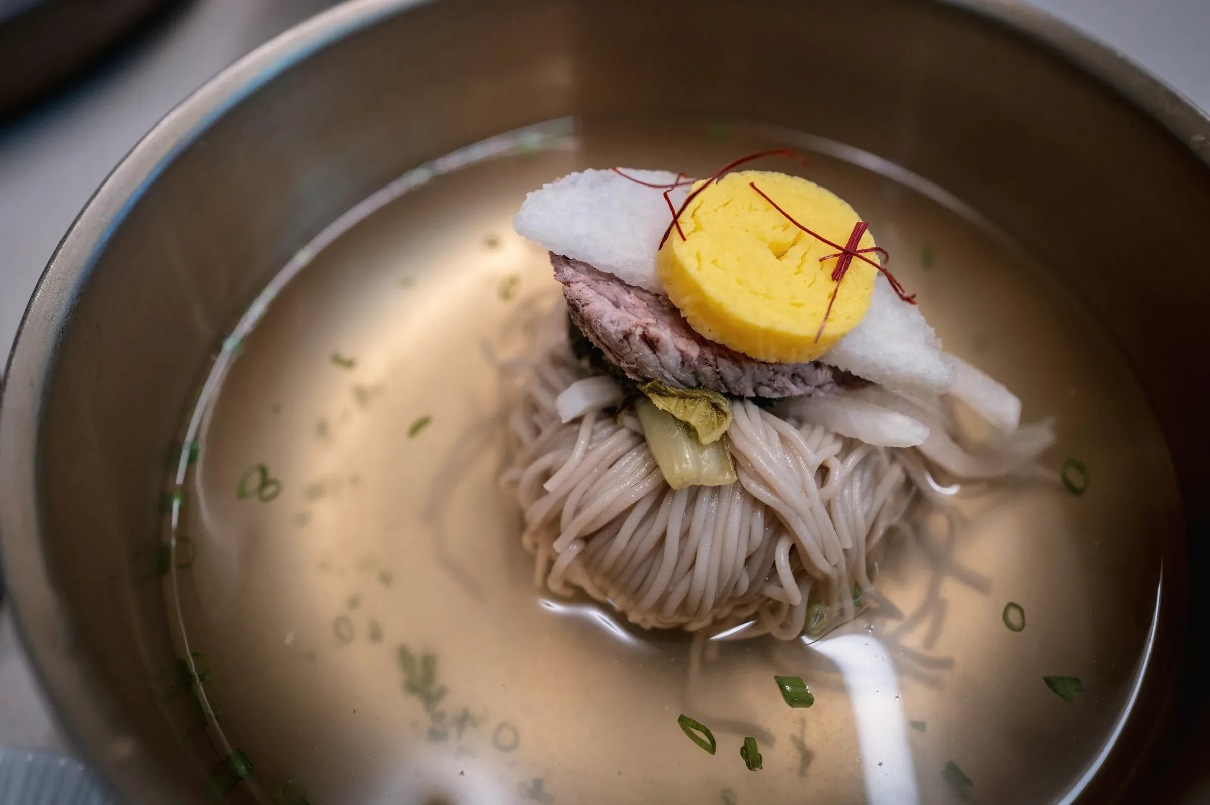 Buckwheat noodles in a clear cold broth under beef, radish, kimchi and a roll of egg, in a steel bowl