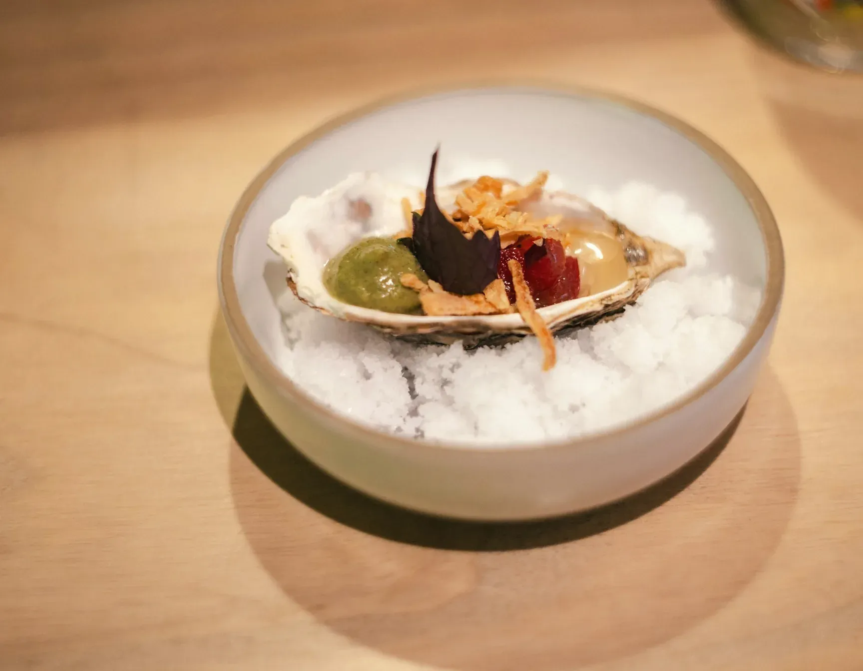 A raw oyster with a little garnish on crushed ice in a small white bowl