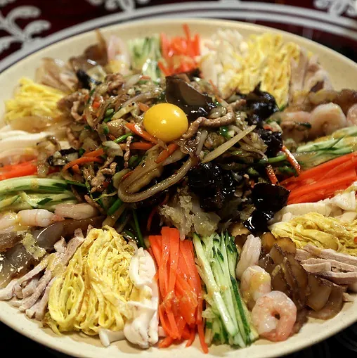A round platter of julienned vegetables, egg, shrimp and pork around a stir-fry, an egg yolk on top